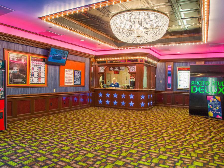 A lobby with a patterned floor, a chandelier, a ticket counter, and a photo studio.