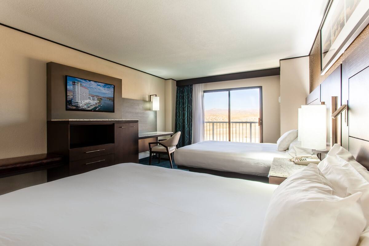 A hotel room with two beds, a desk, a TV, and a window with a view.