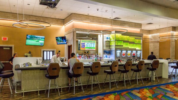 A bar area with a counter, multiple stools, and televisions displaying sports.