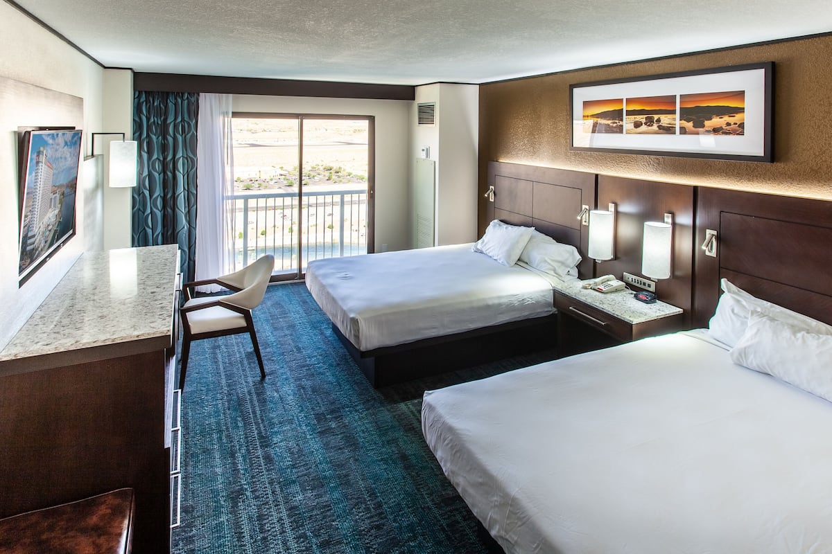 A hotel room with two beds, a desk, a chair, and a balcony with a view.