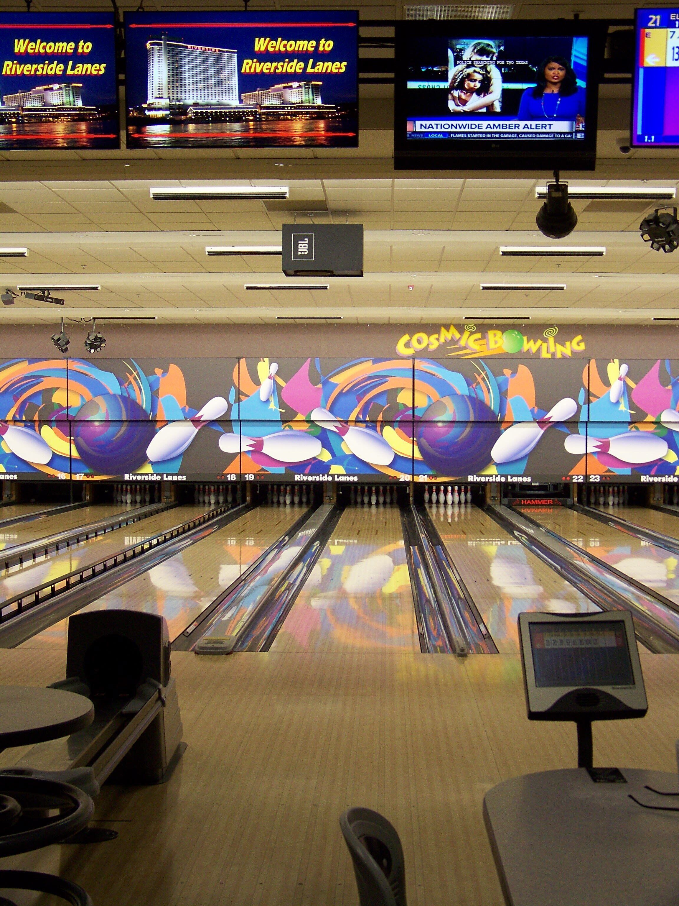 A bowling alley with multiple lanes, a colorful mural, and a welcome sign for Riverside Lanes.