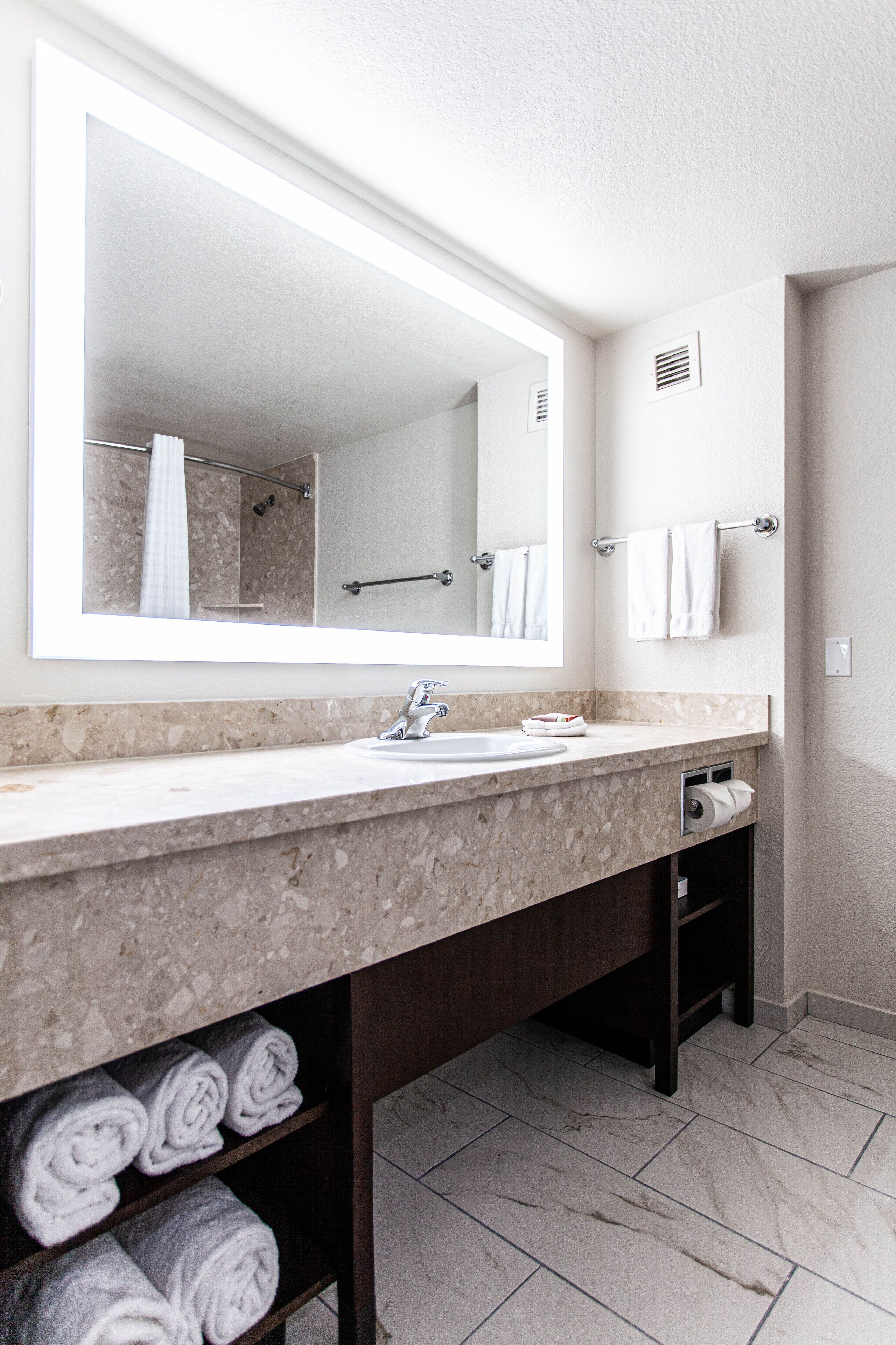 A bathroom with a marble countertop, a large mirror, a sink, and a towel rack.