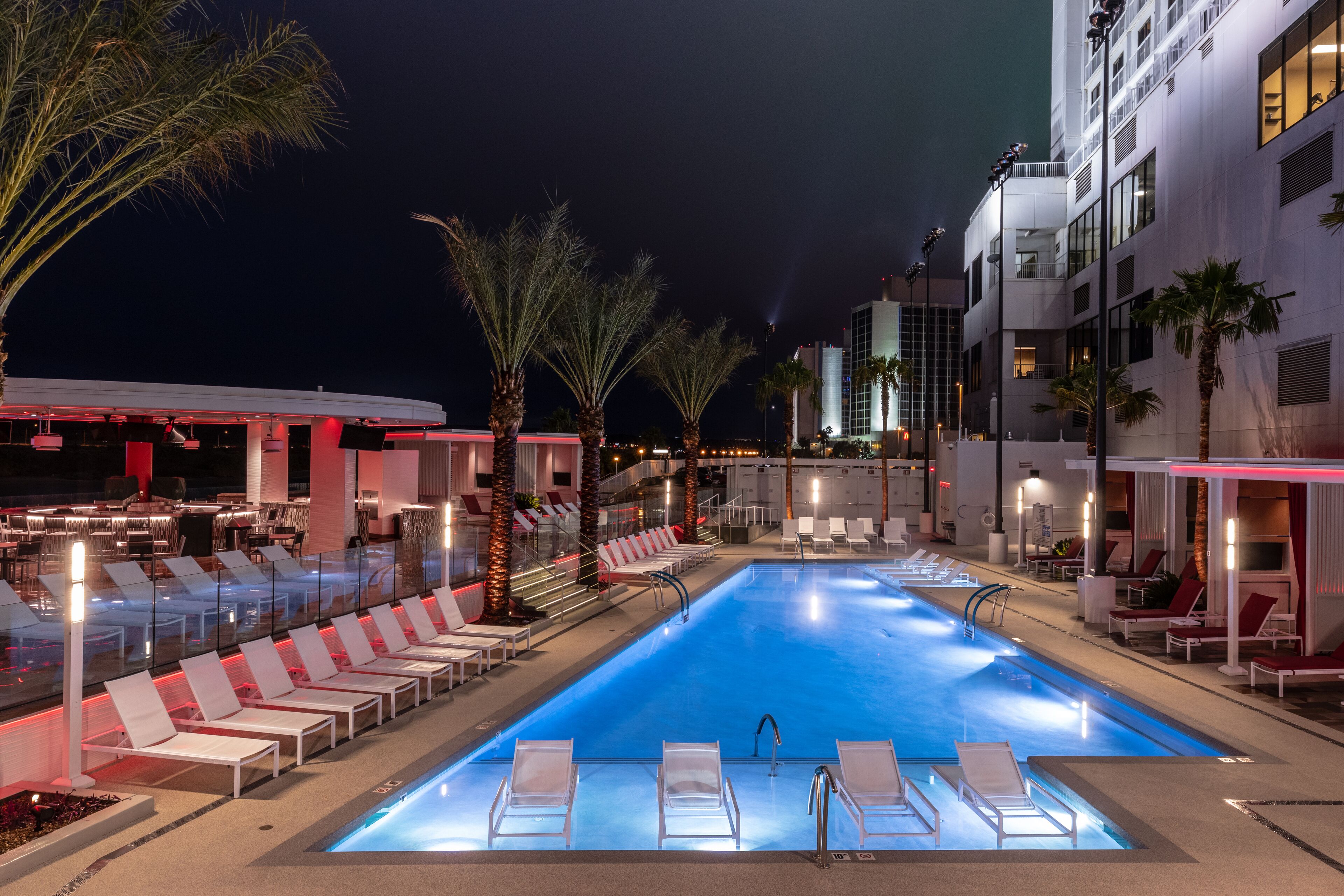 A nighttime swimming pool area with lounge chairs and palm trees.