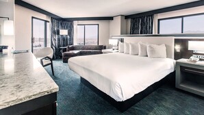 Habitación de hotel con una cama grande, un escritorio, una silla y vistas a la ciudad.
