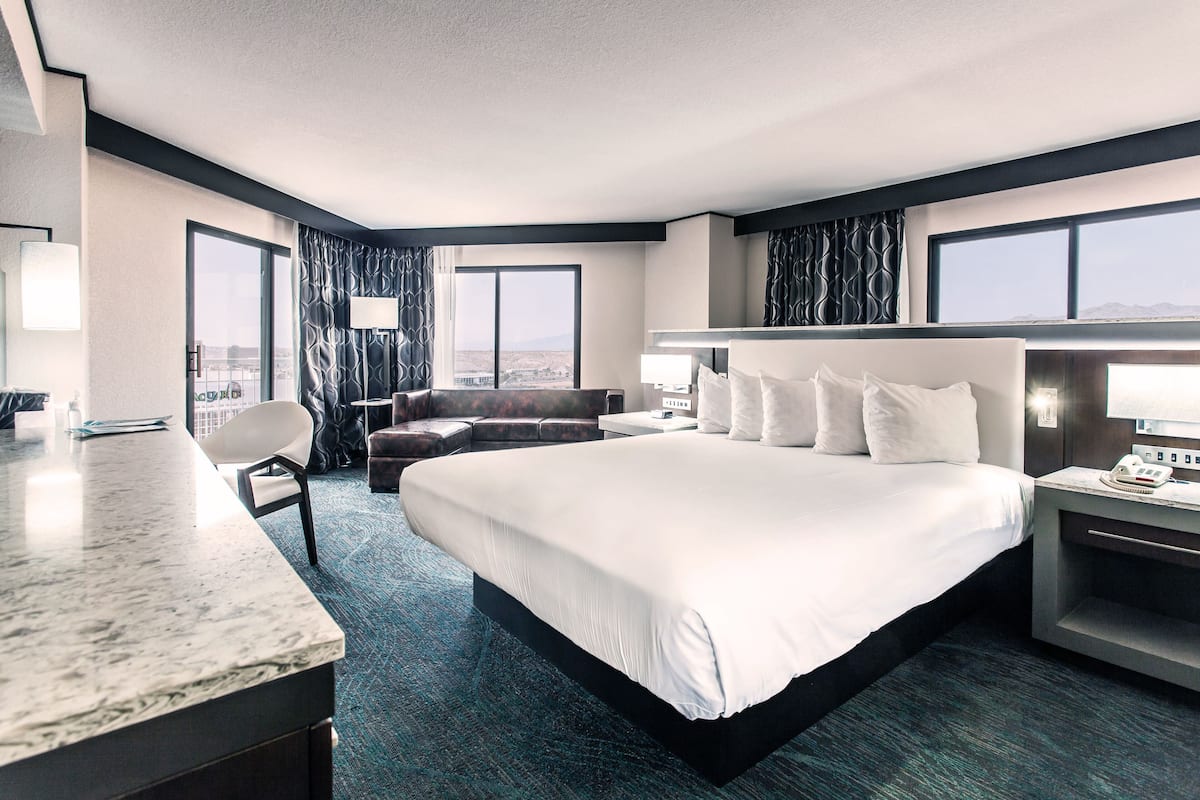 A hotel room with a large bed, a desk, a chair, and a view of the city.