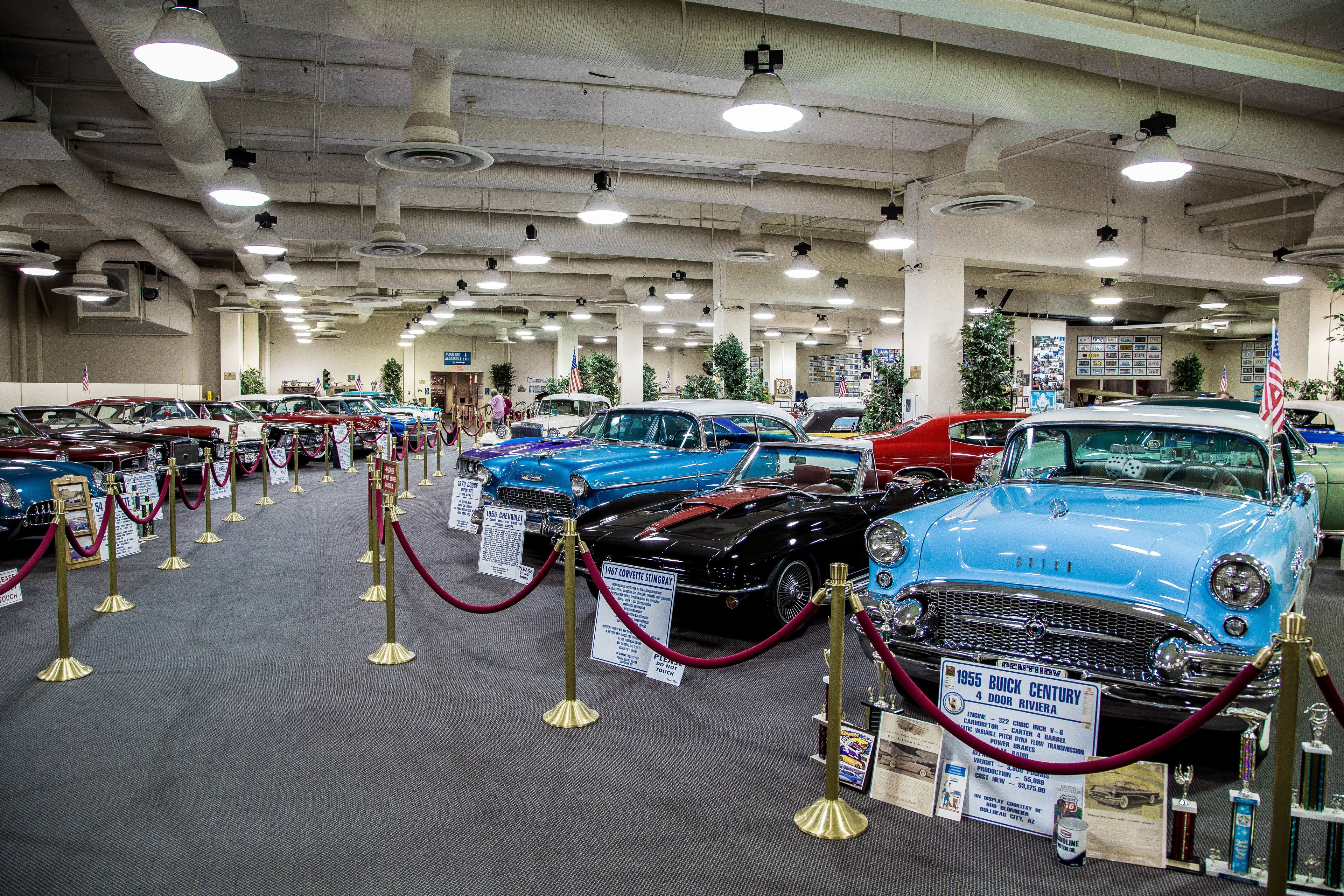 Exposición de automóviles con vehículos clásicos exhibidos, delimitada por una barrera de cuerda roja.