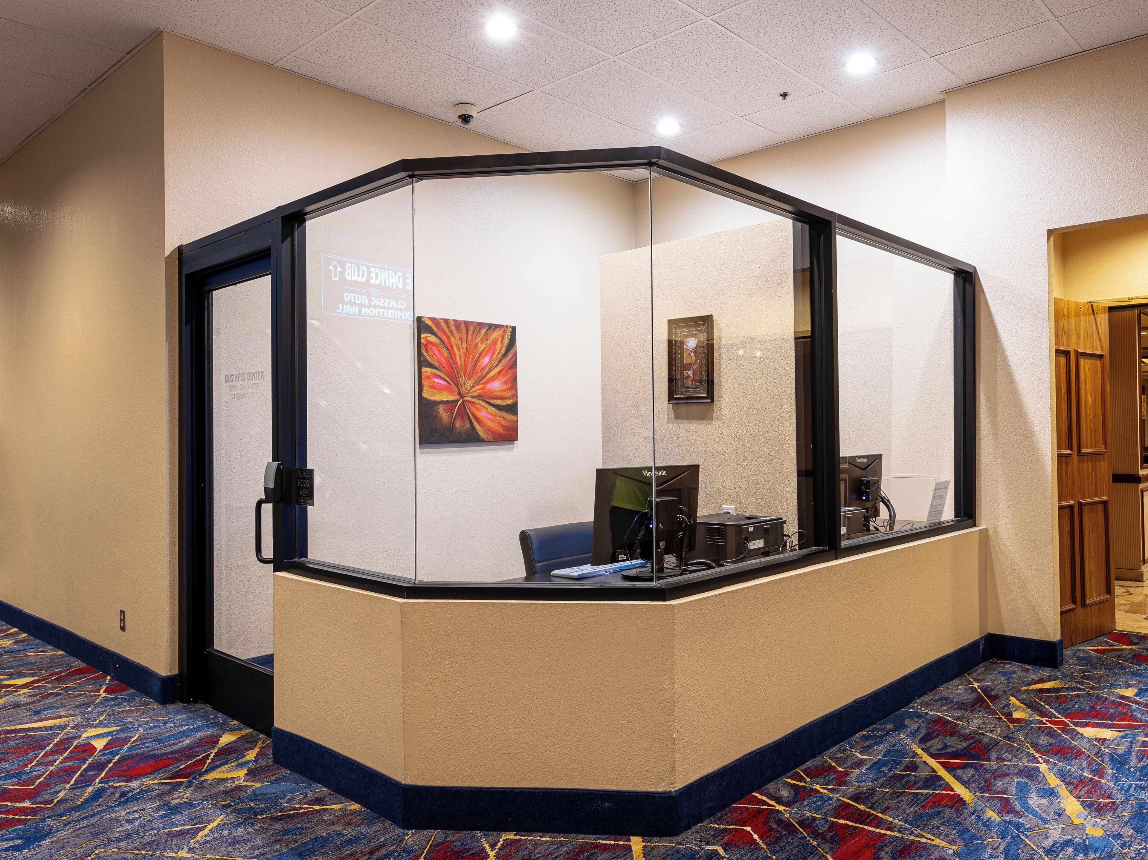 A reception area with a glass partition, a sign indicating 'Business Center', and a colorful carpet.