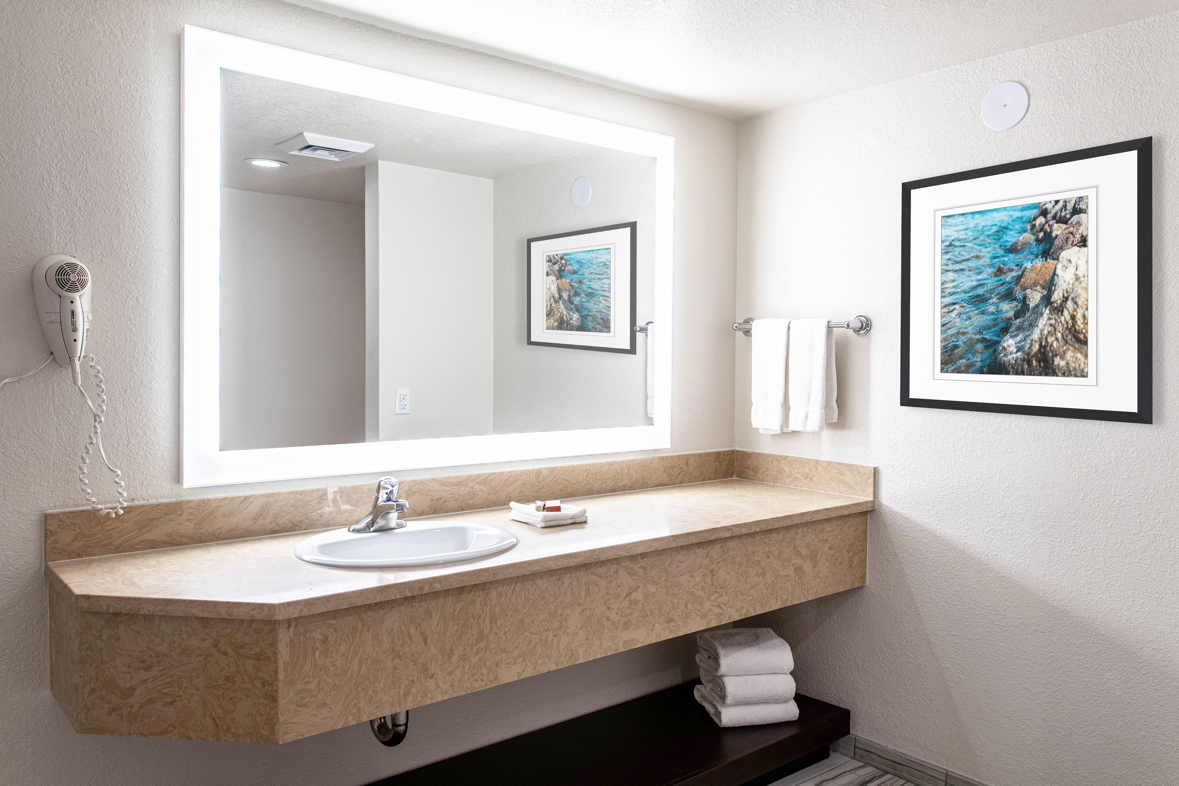 Une salle de bain moderne avec un grand miroir, un lavabo et deux tableaux encadrés accrochés au mur.