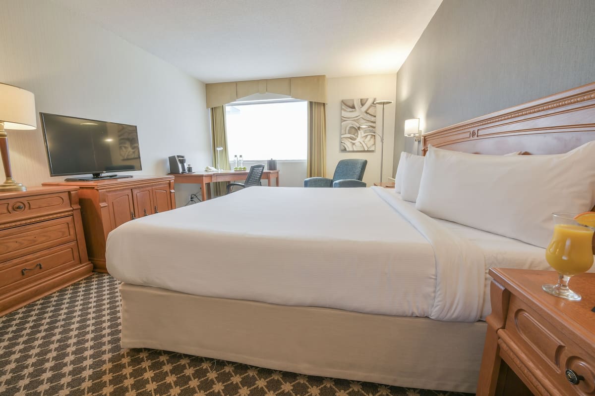 Una habitación de hotel con una cama grande, un escritorio con una silla, un televisor y una lámpara.
