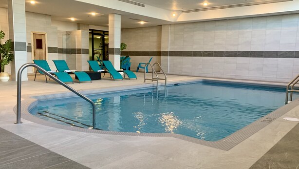 A swimming pool with a tiled deck, lounge chairs, and a fitness area. - Hotel Universel Montreal (Montreal)