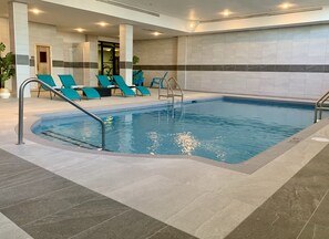Una piscina con solárium empinado, sillas de descanso y un gimnasio.