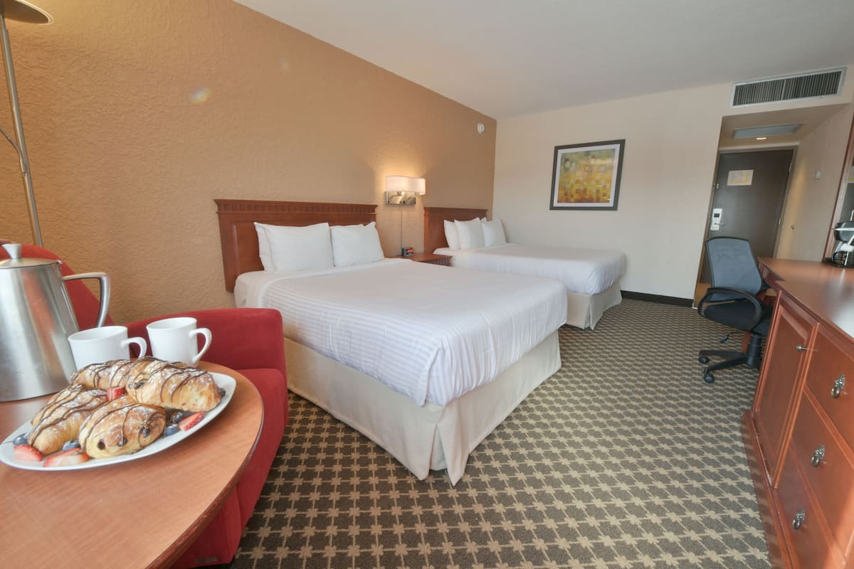 A hotel room with two beds, a dining table with pastries, a coffee pot, and a chair.
