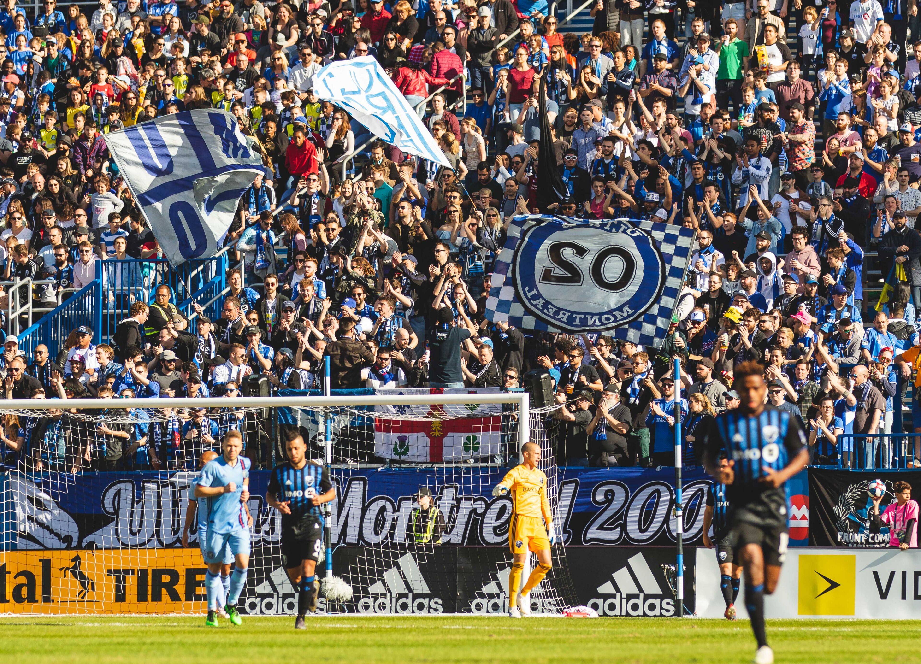 Uno stadio gremito di spettatori, una partita di calcio in corso e striscioni pubblicitari.