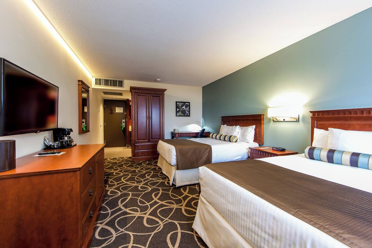 Habitación de hotel con dos camas, televisión, escritorio con cafetera y lámpara de pared.
