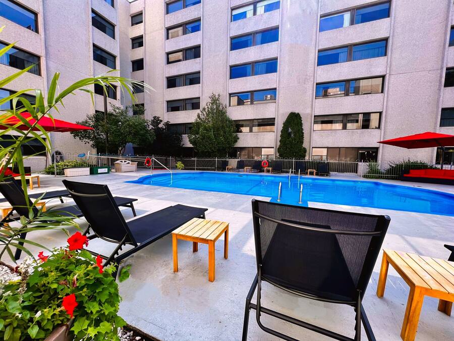 A pool area with lounge chairs and tables, surrounded by a building with multiple floors and windows.