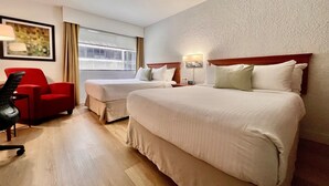 Ein Hotelzimmer mit zwei Betten, einem roten Sessel, einem Schreibtisch und einem Fenster mit Vorhängen.
