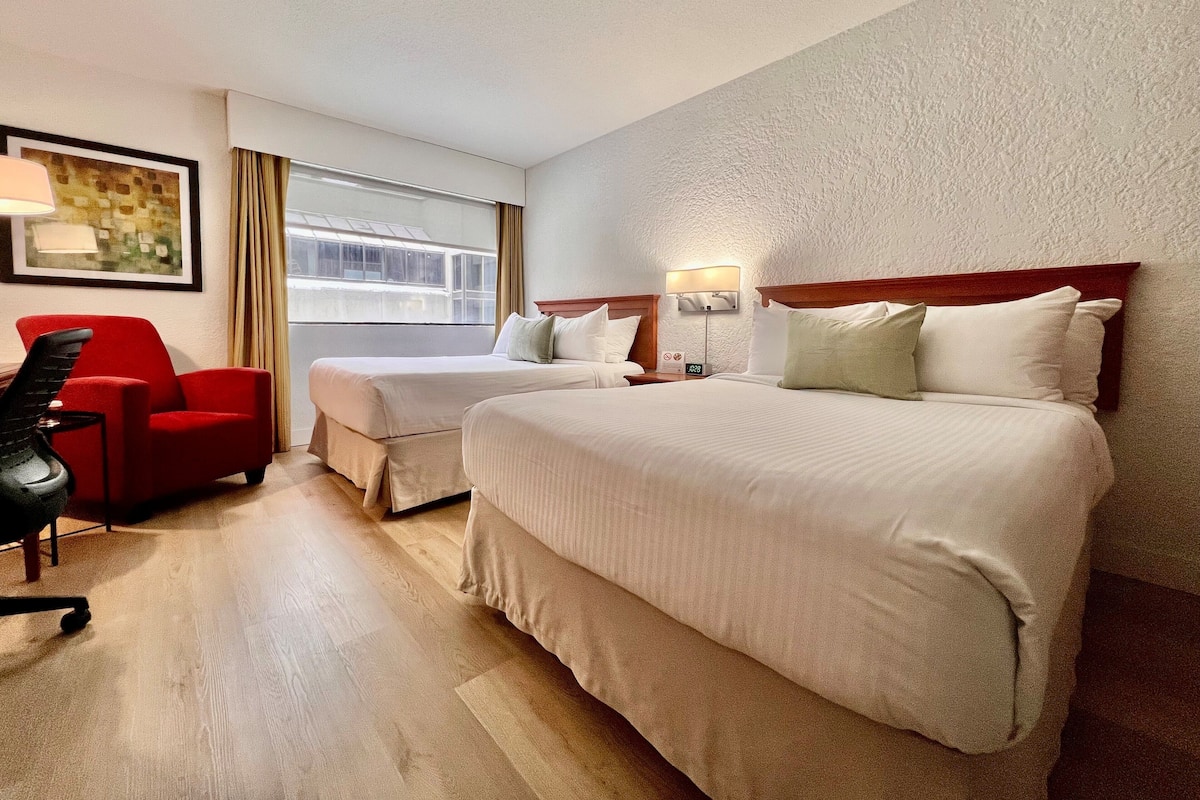 Habitación de hotel con dos camas, un sillón rojo, un escritorio y una ventana con cortinas.