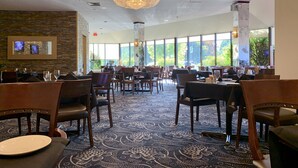 A spacious restaurant with high ceilings, large windows, and a chandelier. Tables are set with plates and glasses. - Hotel Universel Montreal (Montreal)