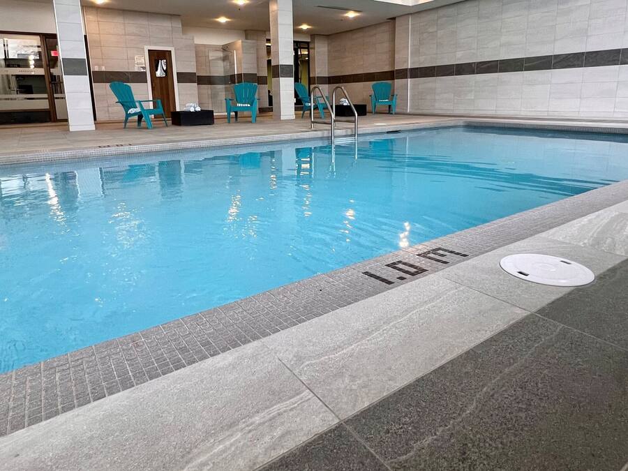 Una piscina con agua cristalina, rodeada de sillas de descanso y un camino empedrado.
