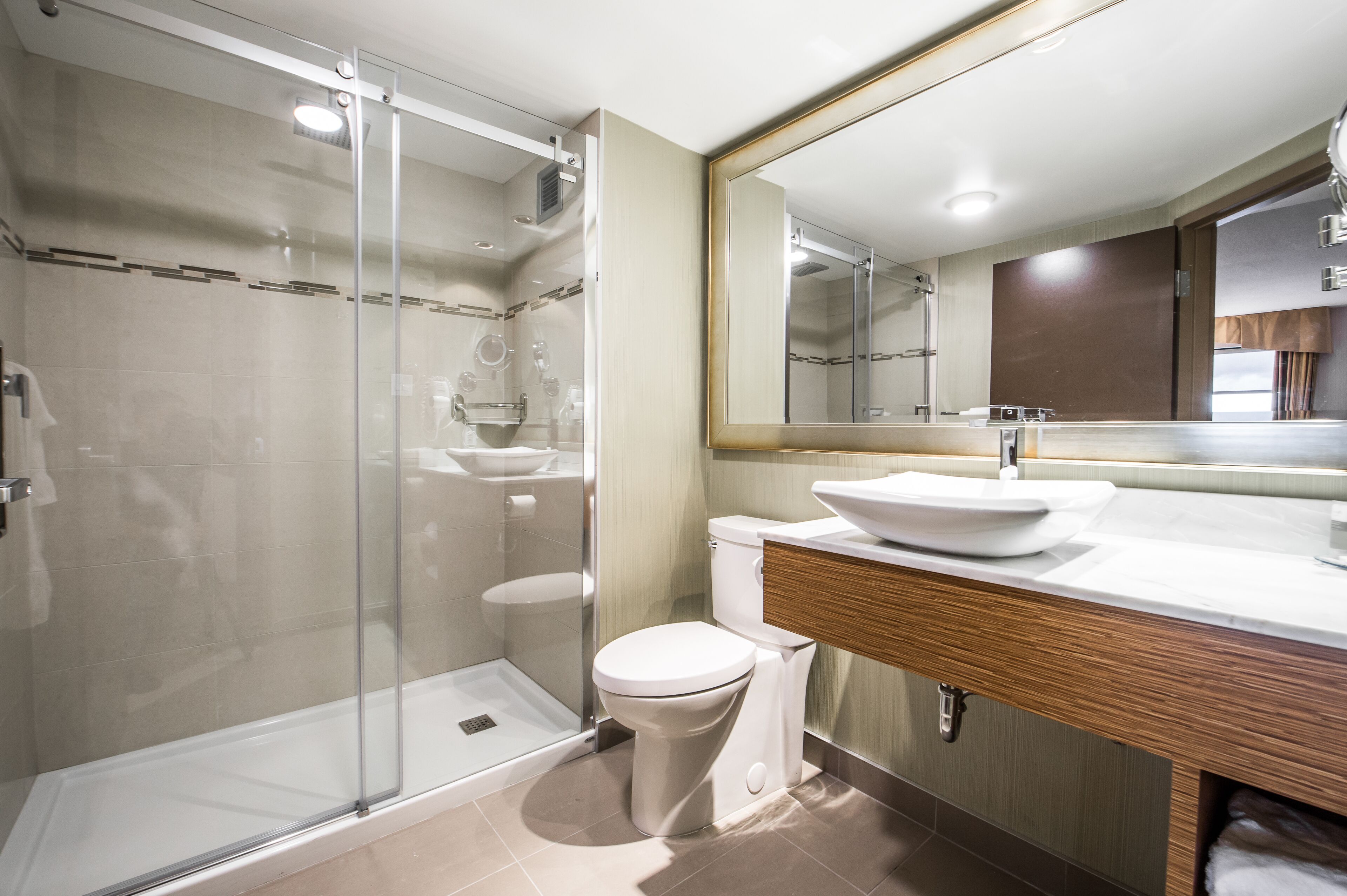 A modern bathroom with a glass-enclosed shower, a white toilet, and a wooden vanity with a large mirror.