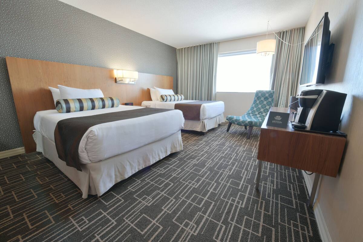 Habitación de hotel con dos camas, un escritorio, un televisor y una ventana con cortinas.