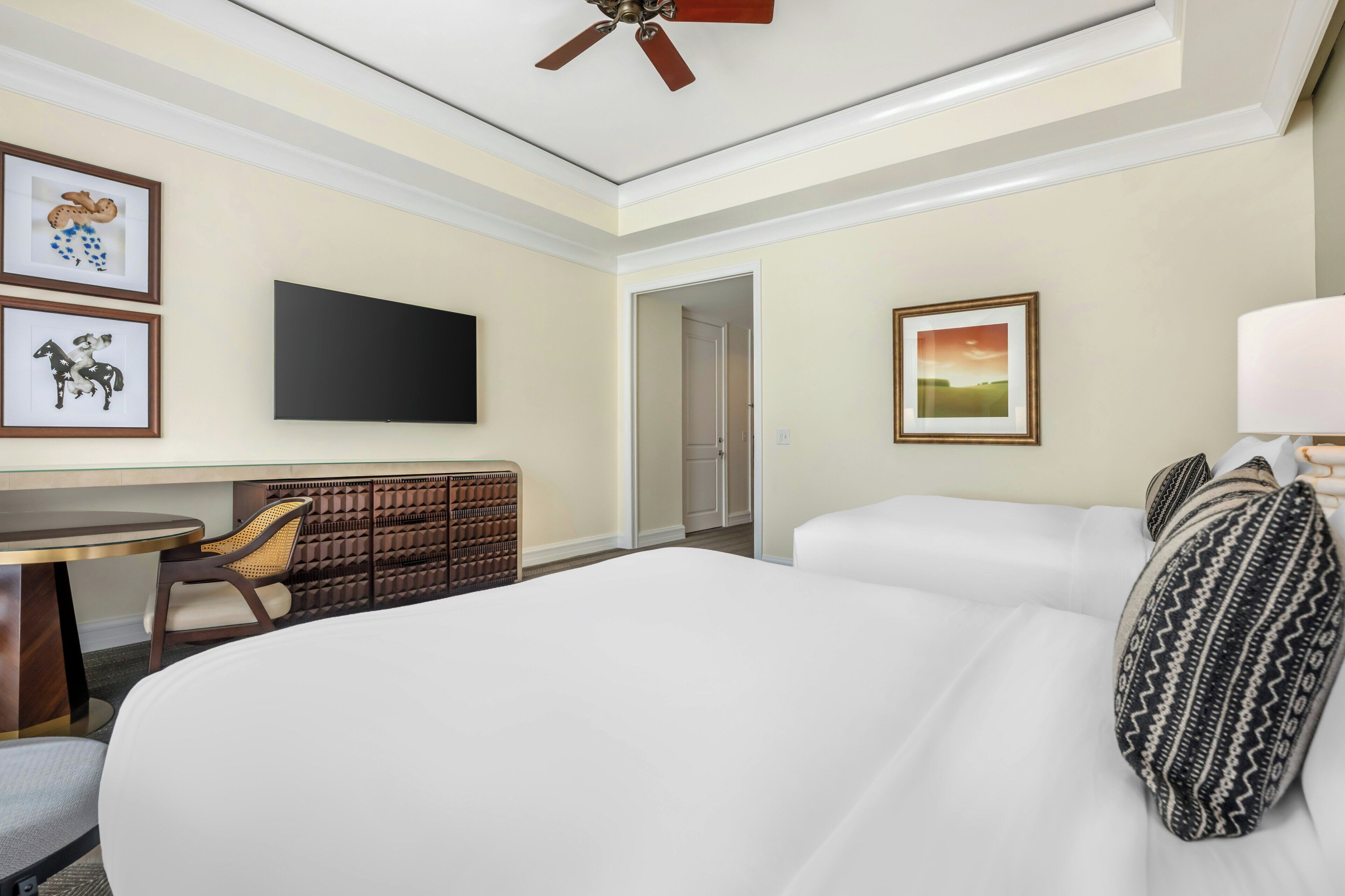 A hotel room with a bed, a desk, a chair, a television, and a door leading to another room.