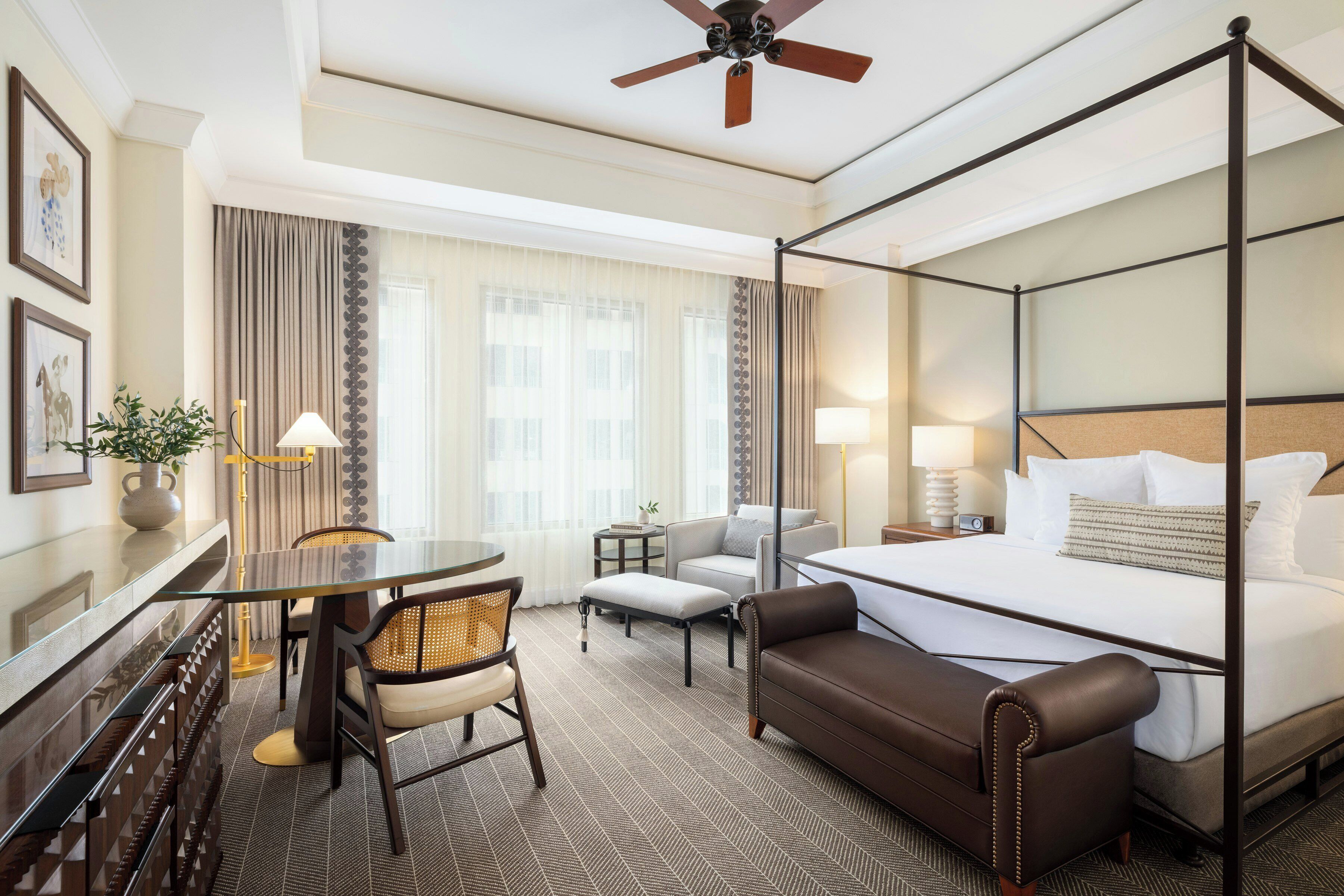 Une chambre d’hôtel avec un lit à baldaquin, un bureau avec une chaise, un canapé et une petite table avec une lampe.