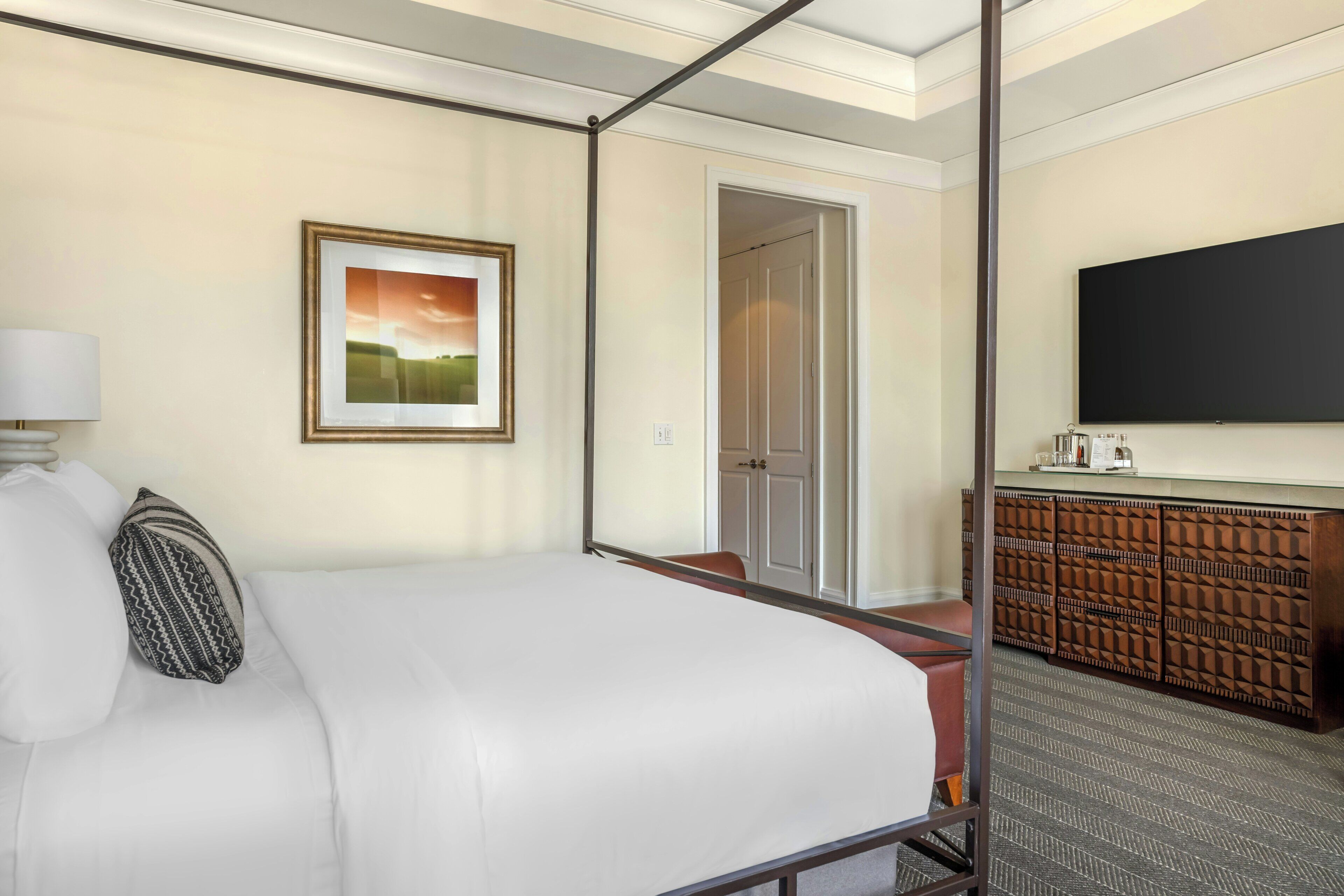 A hotel room with a bed, a bedside lamp, a framed picture, a wardrobe, and a television.