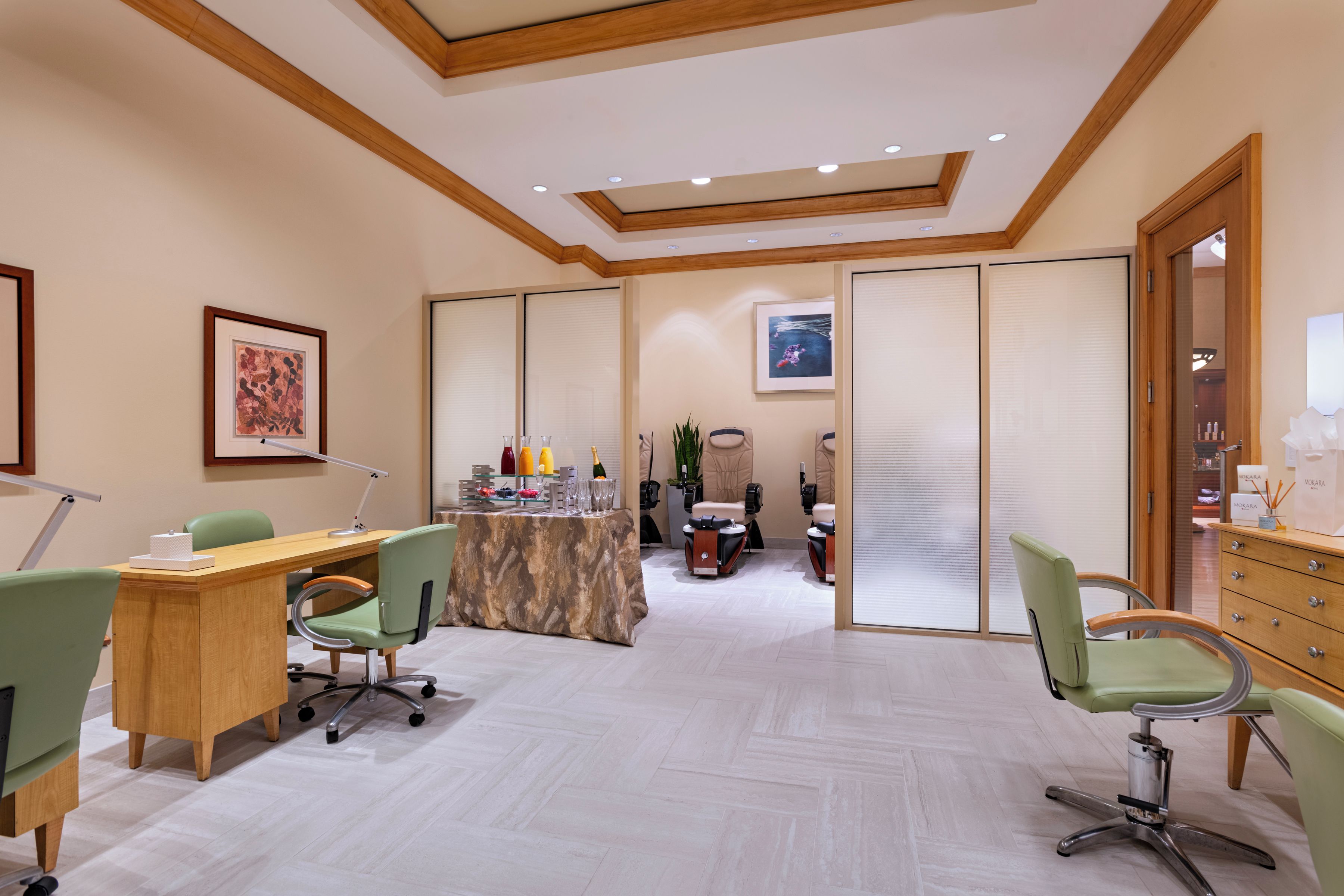 A conference room with a wooden desk, chairs, a table with refreshments, and a view through a partition.