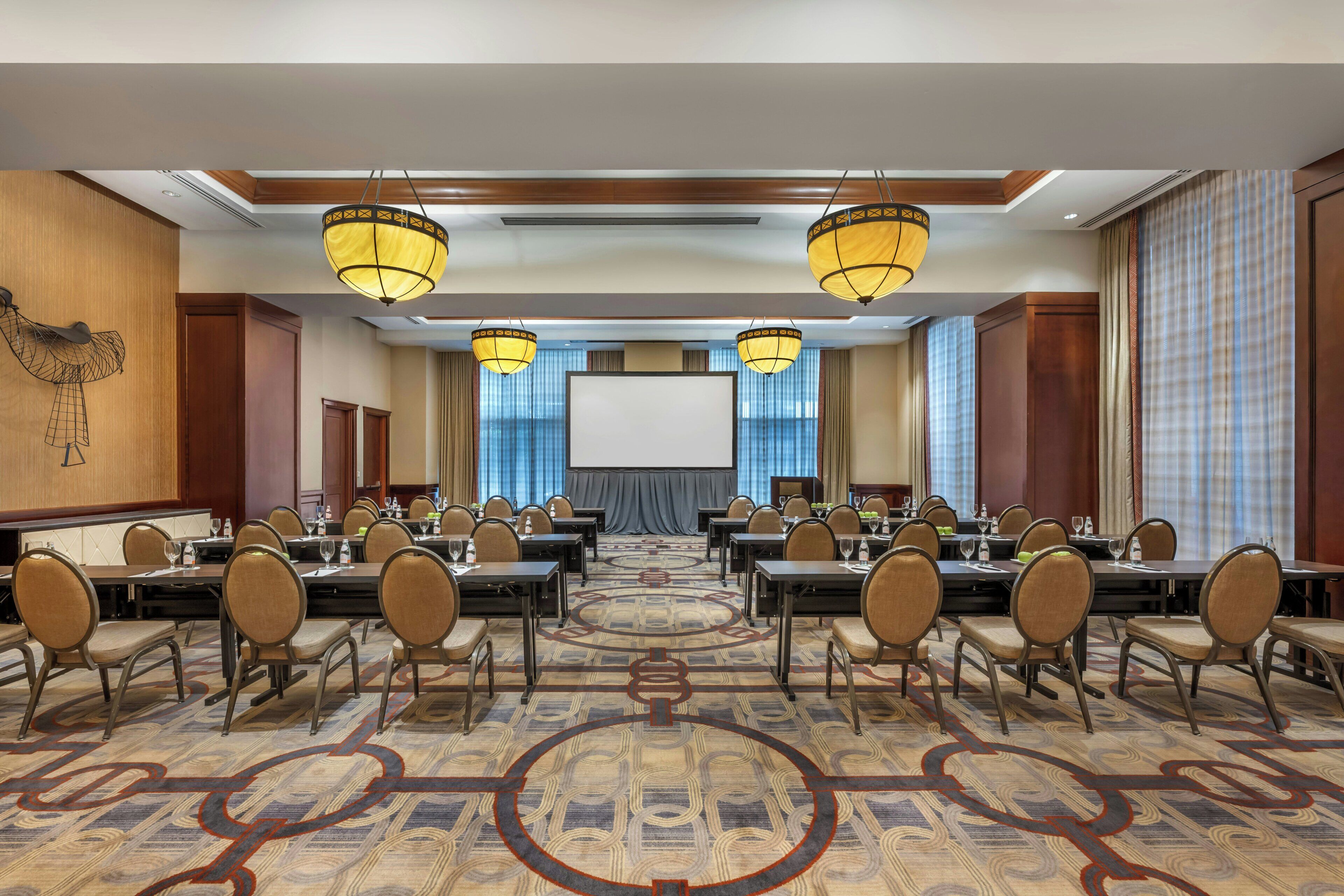 A conference room with multiple tables and chairs, a large screen at the front, and decorative lighting.