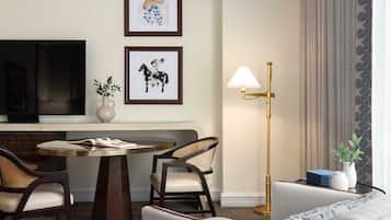 A hotel room with a round table, two chairs, a sofa, a floor lamp, and two framed pictures on the wall.