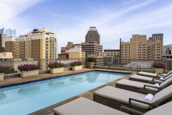 Relax by the rooftop pool with a stunning city view, surrounded by lounge chairs and lush greenery.