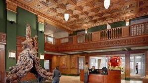 Un vestíbulo con una gran escultura de madera, un mostrador de recepción y un balcón con barandillas ornamentales.