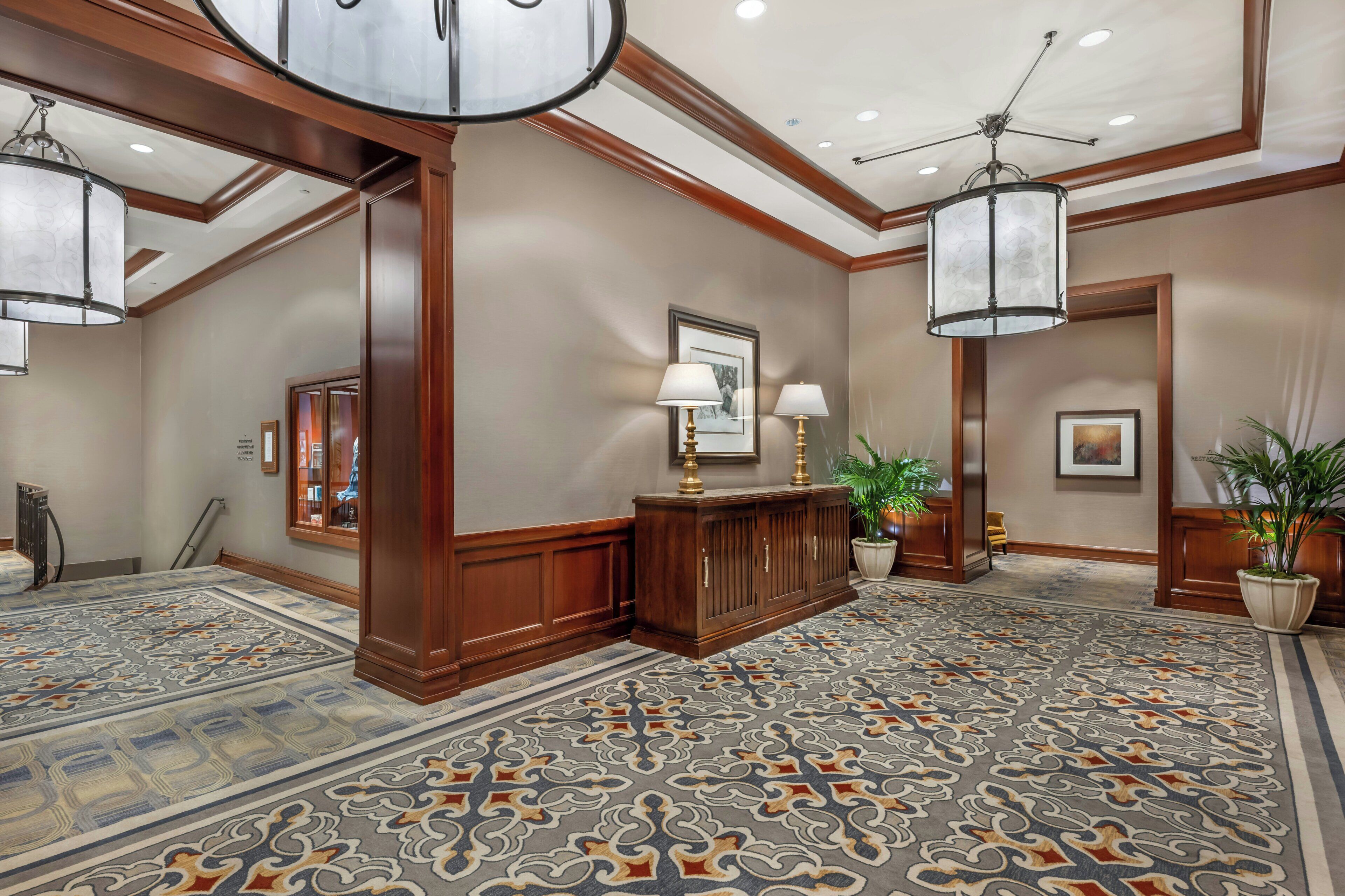 A hotel lobby with a patterned carpet, wooden paneling, a reception desk, and a chandelier.