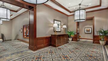 A hotel lobby with a patterned carpet, wooden paneling, a reception desk, and a chandelier.