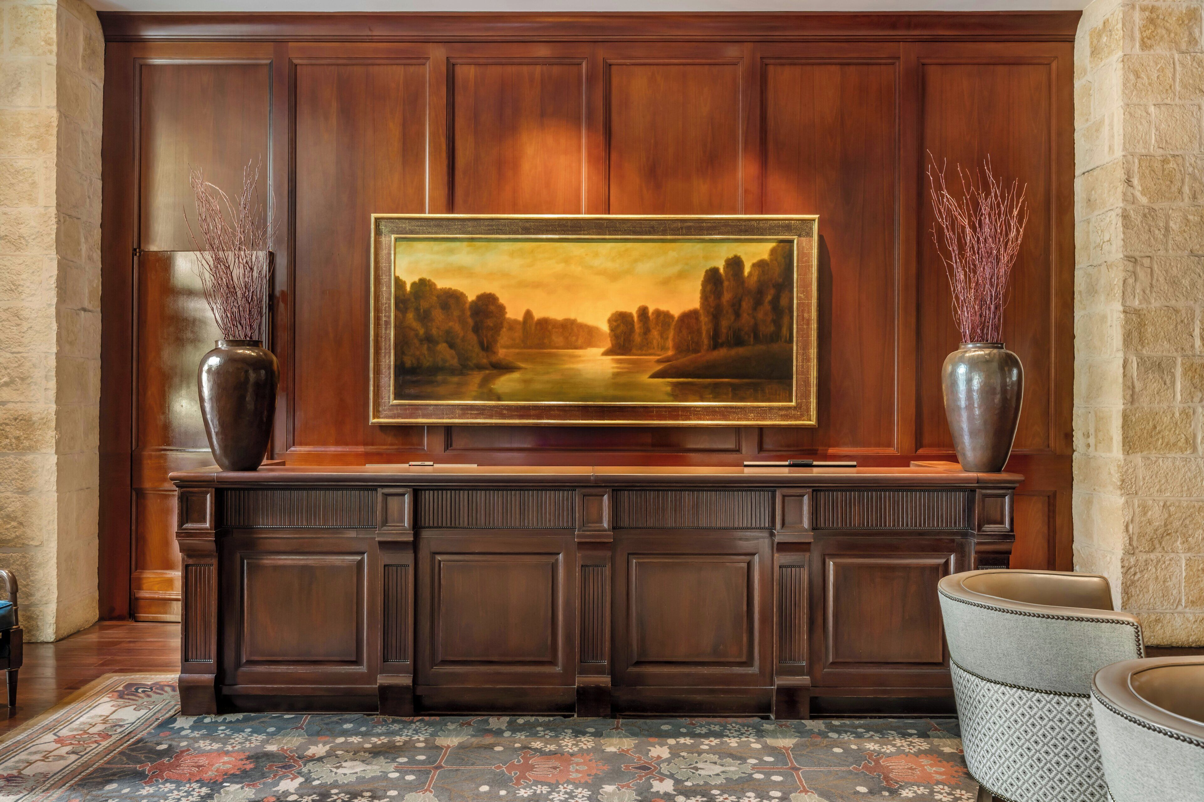 A wooden reception desk with a framed landscape painting above it, flanked by two vases with branches.