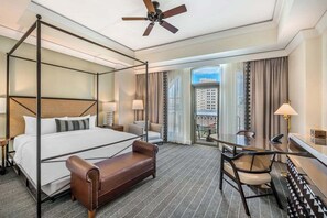 A hotel room with a four-poster bed, a sofa, a dining table with chairs, a desk with a lamp, and a balcony with a view of the city. - Mokara Hotel & Spa San Antonio (San Antonio)