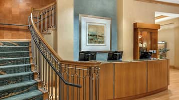 A hotel lobby with a curved reception desk, a staircase with wooden railings, and a framed artwork on the wall.