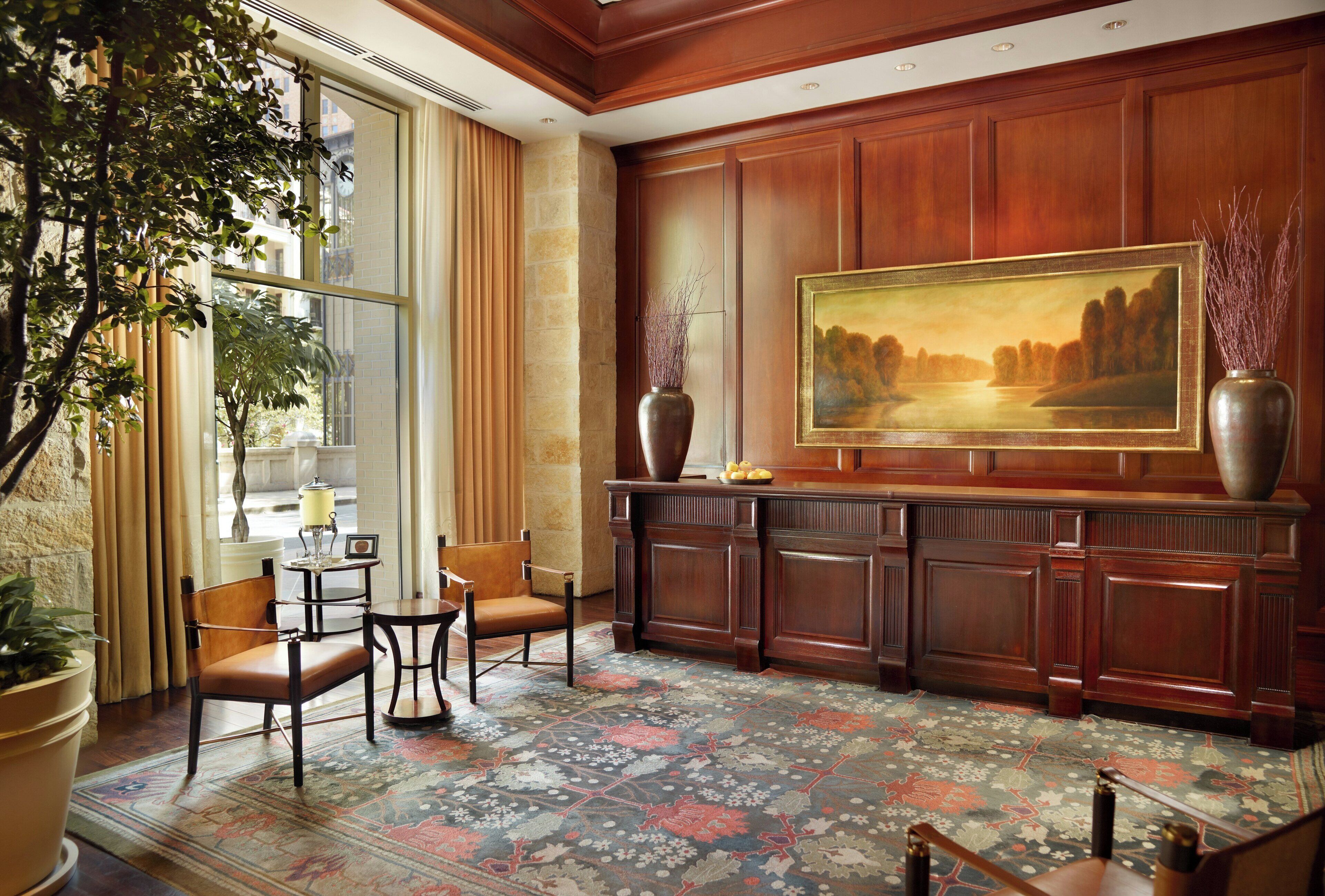 A hotel lobby with a large painting, a fireplace, a seating area with chairs, and a large window with curtains.