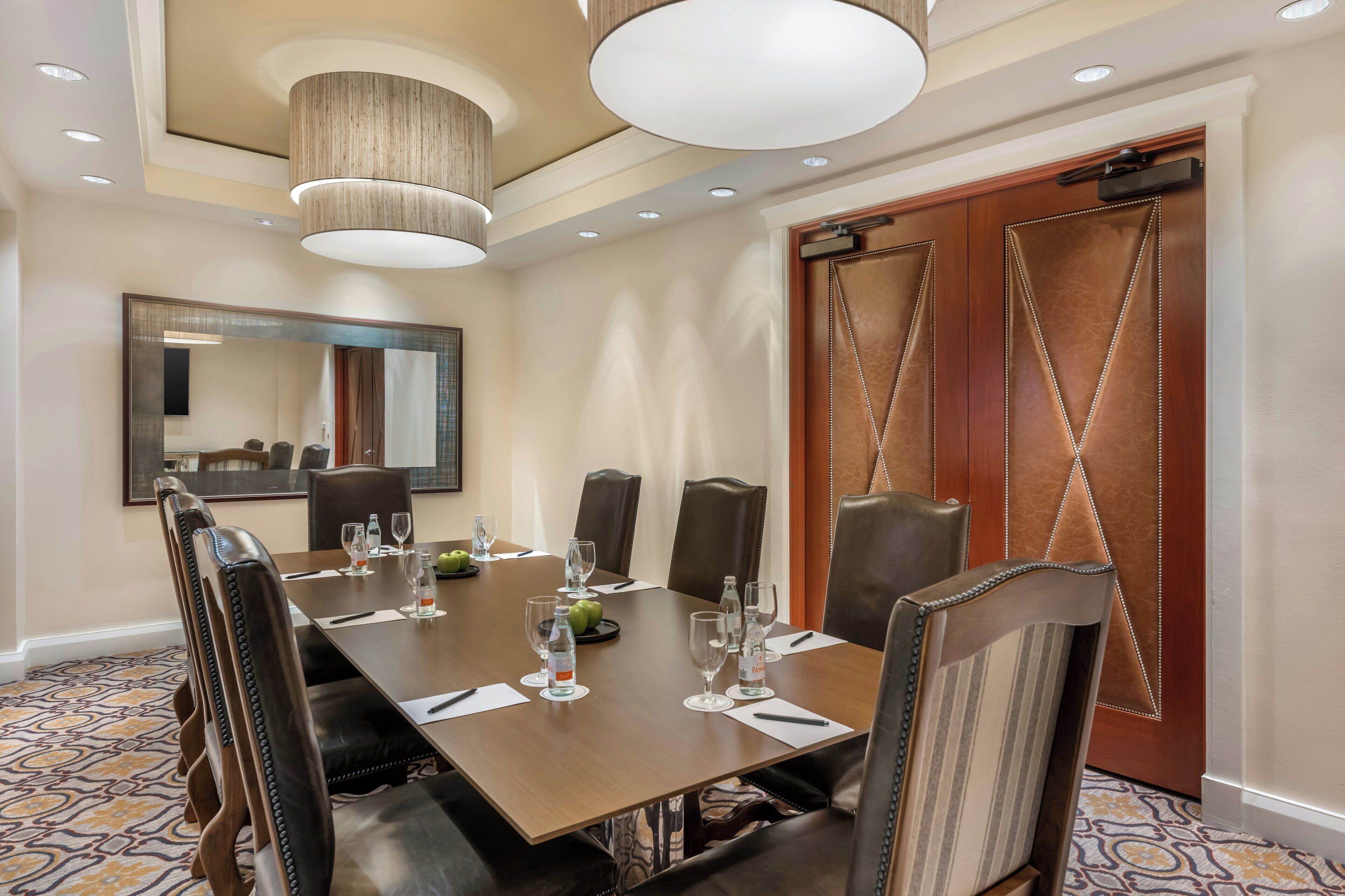 A conference room with a long table, chairs, a mirror, and a door with decorative stitching.