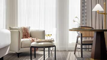 A hotel room with a bed, a sofa, a small table with a tray of glasses and a candle, and a desk with a lamp.