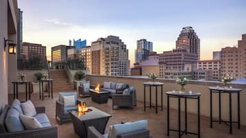 A rooftop terrace with outdoor seating, a fire feature, and a cityscape view.