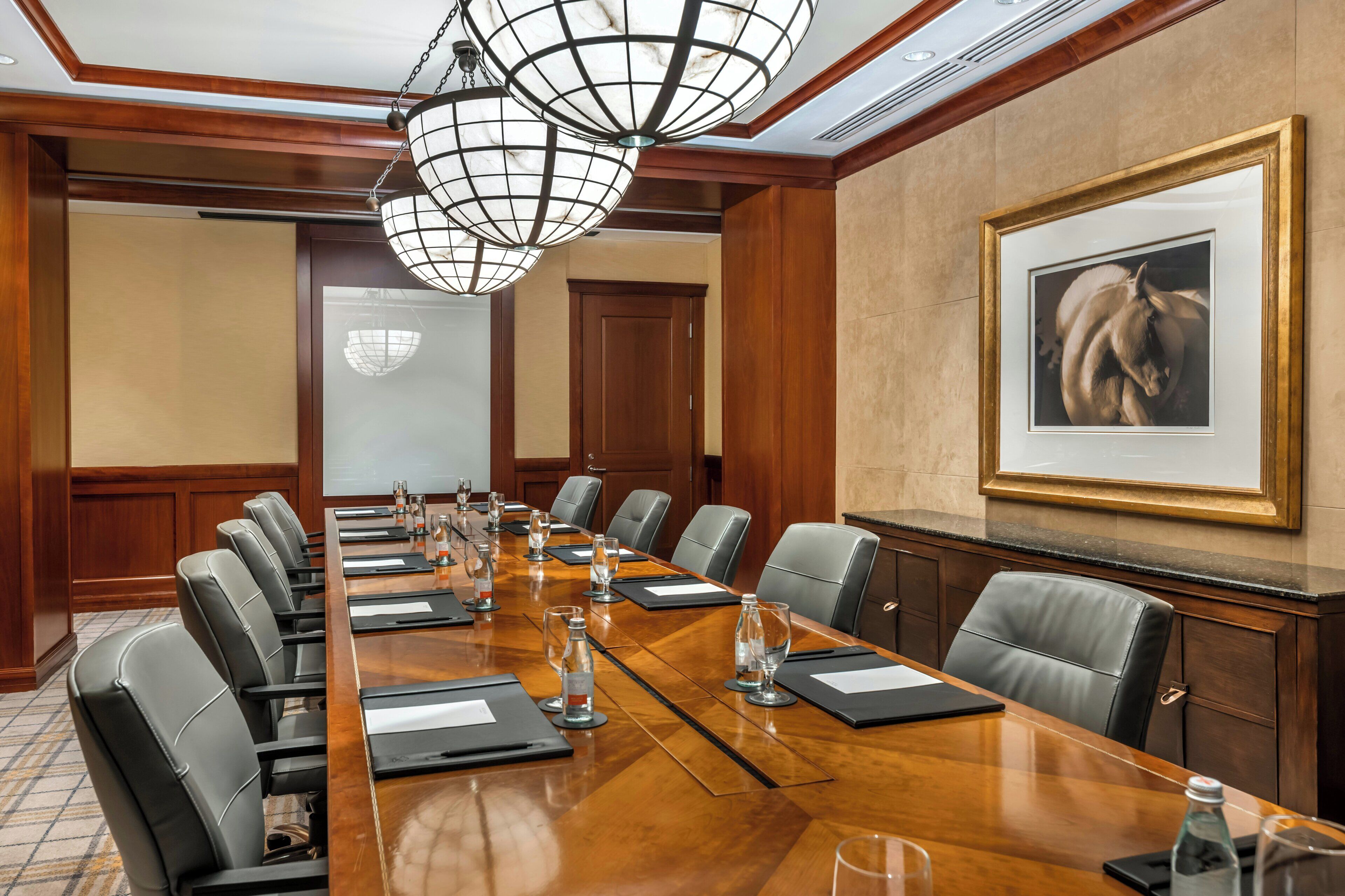 Un salón de conferencias con una larga mesa de madera, sillas de cuero negro y un cuadro grande en la pared.