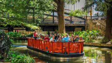 A boat ride with passengers, surrounded by lush greenery and a stone bridge in the background.