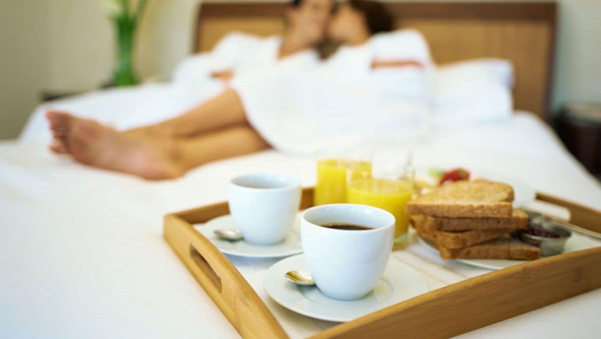 Un plateau de petit-déjeuner avec du café, des toasts et du jus d’orange, posé sur un lit.