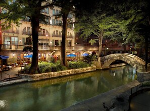 Stroll across the serene courtyard, surrounded by lush greenery and a tranquil water feature, with a classic building in the background.