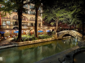Stroll across the serene courtyard, surrounded by lush greenery and a tranquil water feature, with a classic building in the background.