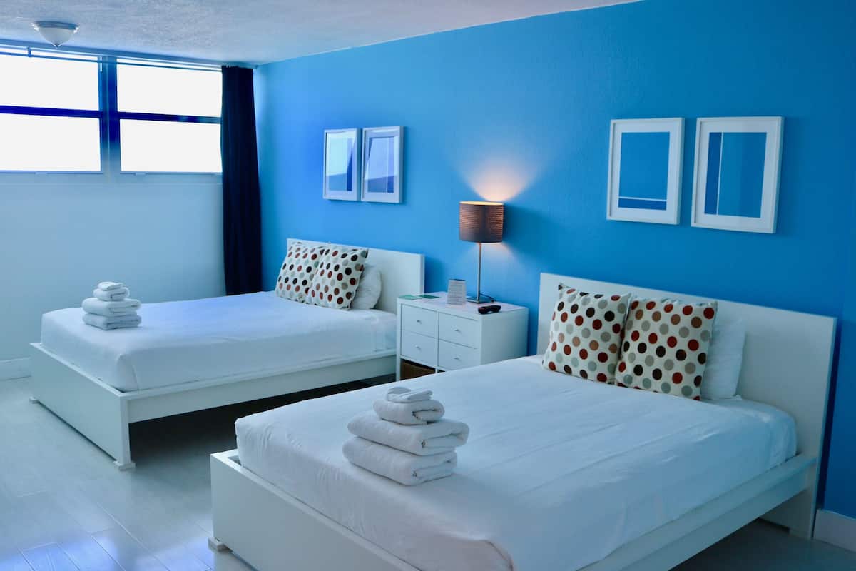A hotel room with two beds, a nightstand, and a lamp.