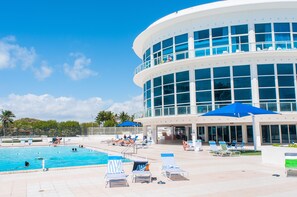 A modern hotel with a swimming pool, sun loungers, and a covered area with umbrellas.