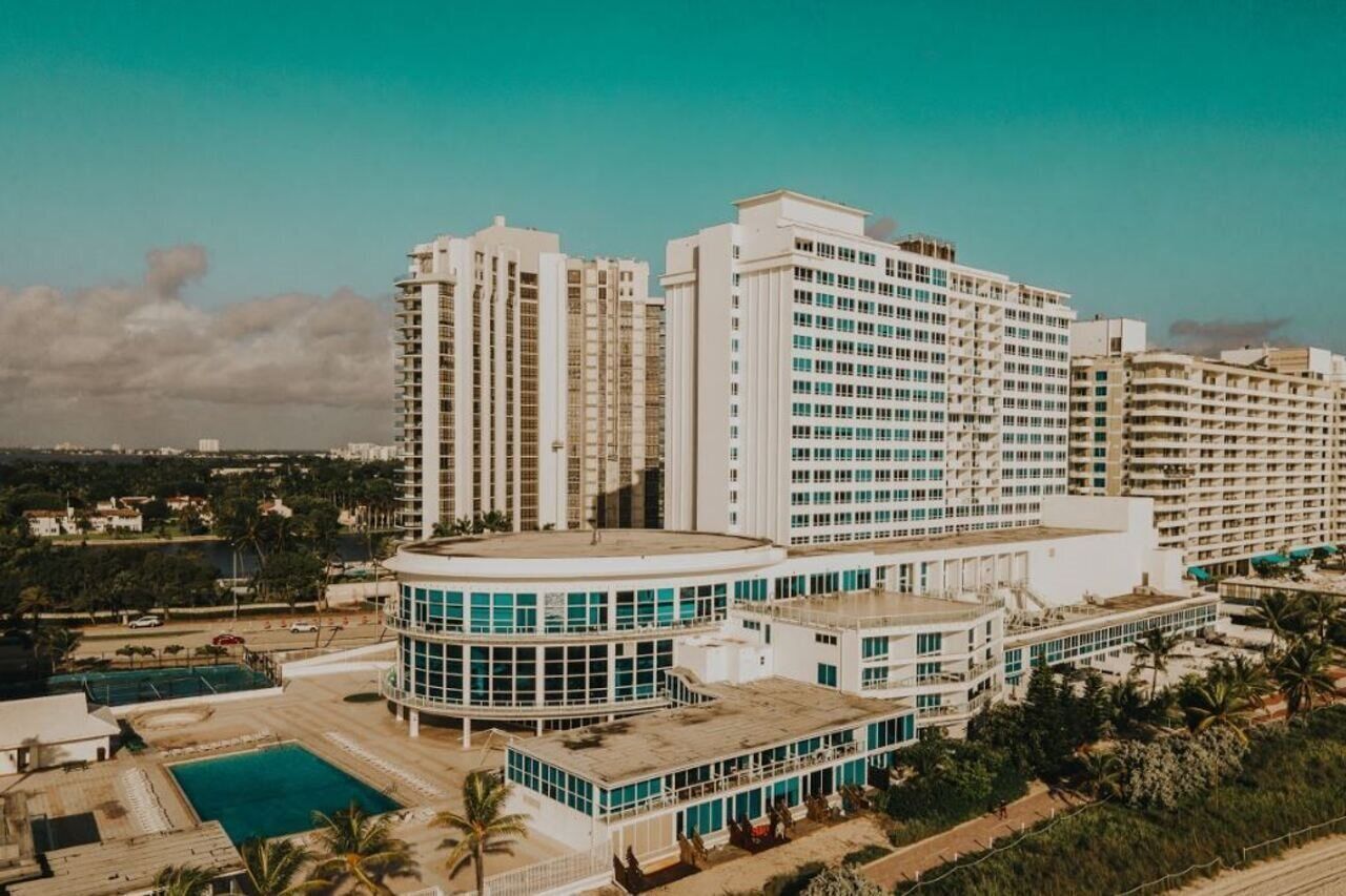 A high-rise hotel with multiple floors, a swimming pool, and a landscaped area with palm trees.